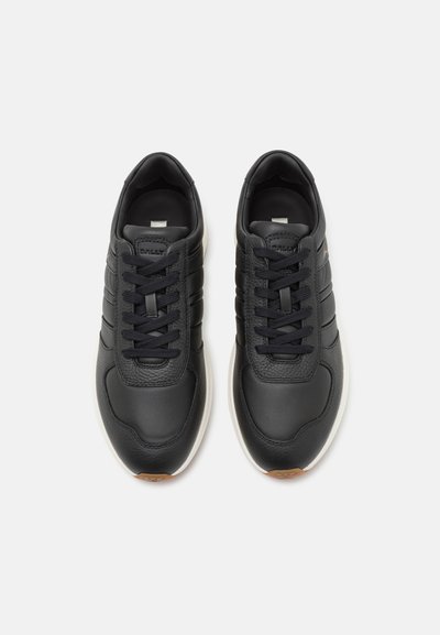 Zapatillas de cuero negro con acentos texturizados, diseño con cordones, mediasuelas blancas y suelas de goma marrón. Presentan tres rayas en el lateral.