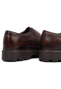 Zapatos de cuero marrón con un acabado texturizado, punta redonda y suela de goma gruesa con surcos profundos para un buen agarre. Diseño con cordones en la parte frontal.