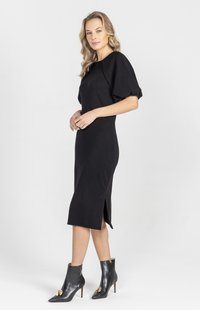 Czarna dzianinowa sukienka o luźnym kroju, z krótkimi bufkami, długości do kolan i z rozcięciem po bokach. Do tego czarne szpiczaste botki na kostkę ze złotymi akcentami.