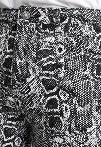 Pantalones de mezclilla con estampado de serpiente en blanco y negro, de diseño ajustado, con cierre de botón y un patrón texturizado detallado.