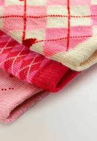 Drei zusammen gerollte Strickstoffe. Merkmale sind rosa Farbtöne mit Mustern: Argyle, Streifen und Herzen. Weicher Textur, unterschiedliche Tiefen.