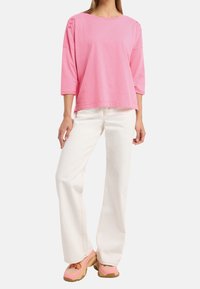 Rosa randig topp med trekvartsärmar, kombinerad med vita vida jeans och kraftiga, flerfärgade sneakers.