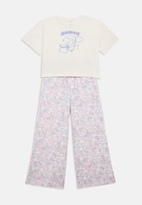 Cremfarbener Crop-Top mit blauer Grafik eines Charakters, kombiniert mit pinken Schlafanzughosen, die ein sich wiederholendes, verspieltes Charaktermuster zeigen.