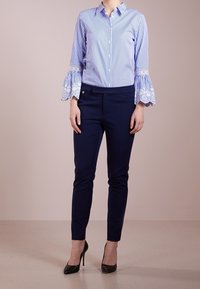Randig blå och vit skjorta med volangspetsärmar, parat med figursydda marinblå byxor och svarta högklackade skor. Enkel, skräddarsydd design.