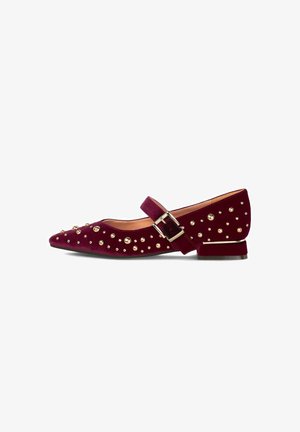 Zapato Mary Jane de terciopelo burdeos con tachuelas doradas, puntera puntiaguda, correa con hebilla dorada y tacón bajo con ribete dorado.