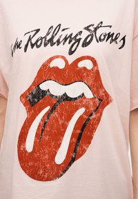 Ξεθωριασμένο λογότυπο των Rolling Stones με κόκκινα χείλη και γλώσσα σε απαλό ροζ ύφασμα μπλουζακιού.