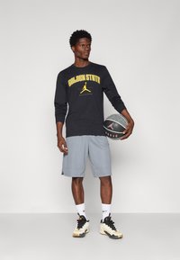 Svart langermet skjorte med "GOLDEN STATE" i gult, grå treningsshorts, svarte joggesko med gull detaljer, og en basketball.