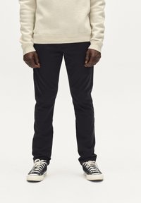 Pulover deschis la culoare și pantaloni negri, mulți. Pantalonii au o textură fină și sunt asortați cu adidași alb-negru.