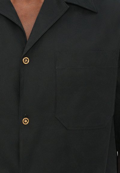 Chemise noire à boutons avec une poche sur le côté gauche, boutons jaunes, manches courtes et un tissu lisse et texturé.