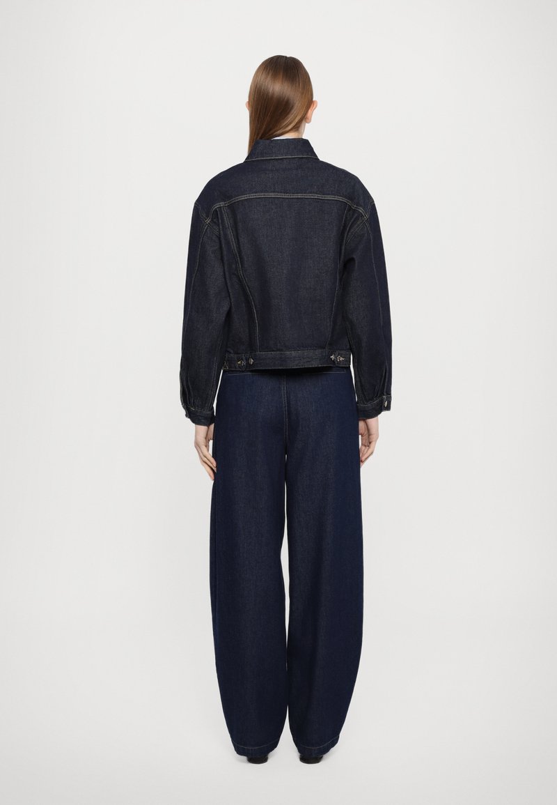 Giubbotto in denim scuro con vestibilità leggermente corta, abbinato a pantaloni in denim scuro a gamba larga. Presenta chiusure con bottoni e tasche laterali.