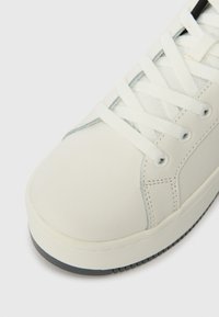 Witte sneaker met bovenwerk van glad leer, ronde neus en witte veters. Heeft grijze accenten en een gestructureerde witte rubberen zool voor grip.