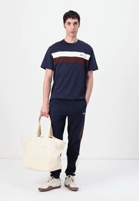 Μπλούζα navy με λευκές και μπορντό ρίγες, συνδυασμένη με navy φόρμες. Το μοντέλο κρατάει μια εκρού τσάντα. Casual αθλητικά παπούτσια.