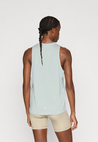 Γαλάζιο αμάνικο αθλητικό τοπ με υφή, με επιμηκυμένη πλάτη, φορεμένο με μπεζ σορτς.