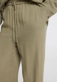Pantalons vert olive clair en tissu doux et texturé, dotés d'une taille élastique avec cordon de serrage et de poches latérales.
