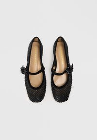 Ballerines noires avec une tige texturée ornée de petits bijoux, bout rond et une sangle décorative avec une boucle. Semelle en cuir.