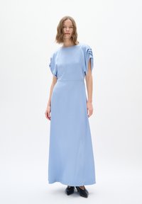 Abito maxi azzurro chiaro con maniche corte arricciate e una vestibilità rilassata. Tessuto morbido, lungo fino al pavimento, abbinato a scarpe nere a punta.