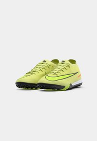 Jasne žlté športové topánky s textúrovaným zvrškom, čiernou podrážkou a výrazným čiernym logo Nike. Majú šnúrky a nízky profil.