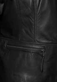 Schwarze Lederjacke mit einem vertikalen Nahtdesign und einer Reißverschlusstasche auf der Vorderseite. Glatte Textur mit einem eleganten Finish.