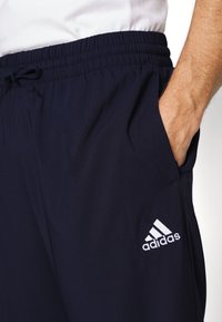Navy blue jogging pants made of lightweight fabric, featuring an elastic waistband, drawstring, side pockets, and a white Adidas logo.