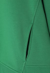 Felpa verde caratterizzata da un tessuto testurizzato, dettagli delle cuciture sottili e una tasca angolata sul lato inferiore per la funzionalità.