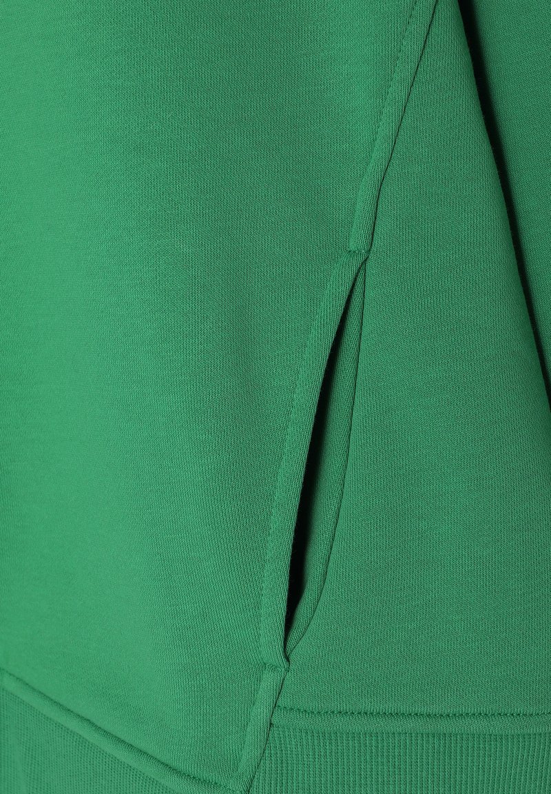 Zielona bluza z materiału o fakturze, subtelnym przeszyciem oraz kątem kieszeni po stronie dolnej dla lepszej funkcjonalności.