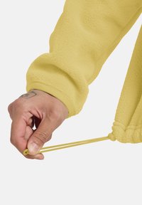 Pullover in fleece giallo con superficie texturizzata; mano che tira un cordino con un fermaglio all'orlo; polsini elastici lisci a contrasto.