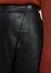 Černá kožená sukně s hladkou strukturou, zdobená dvěma kovovými knoflíky na pase a precizními šicími detaily.