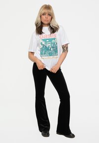 White t-shirt with an Oasis graphic and text in pink and yellow, paired with black velvet flared trousers and black shoes.