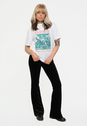 White t-shirt with an Oasis graphic and text in pink and yellow, paired with black velvet flared trousers and black shoes.