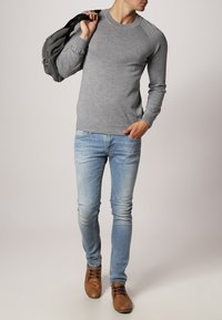Grauer Strickpullover mit rundem Halsausschnitt, kombiniert mit hellblauen Jeans und braunen Schnürschuhen. Der Pullover hat gerippte Ärmelabschlüsse und einen gerippten Saum.