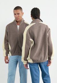 Fleece zip-up jack in bruin en roomkleur met een gestructureerd oppervlak, hoge kraag en een relaxed fit. Heeft verlengde schouders en zijzakken.