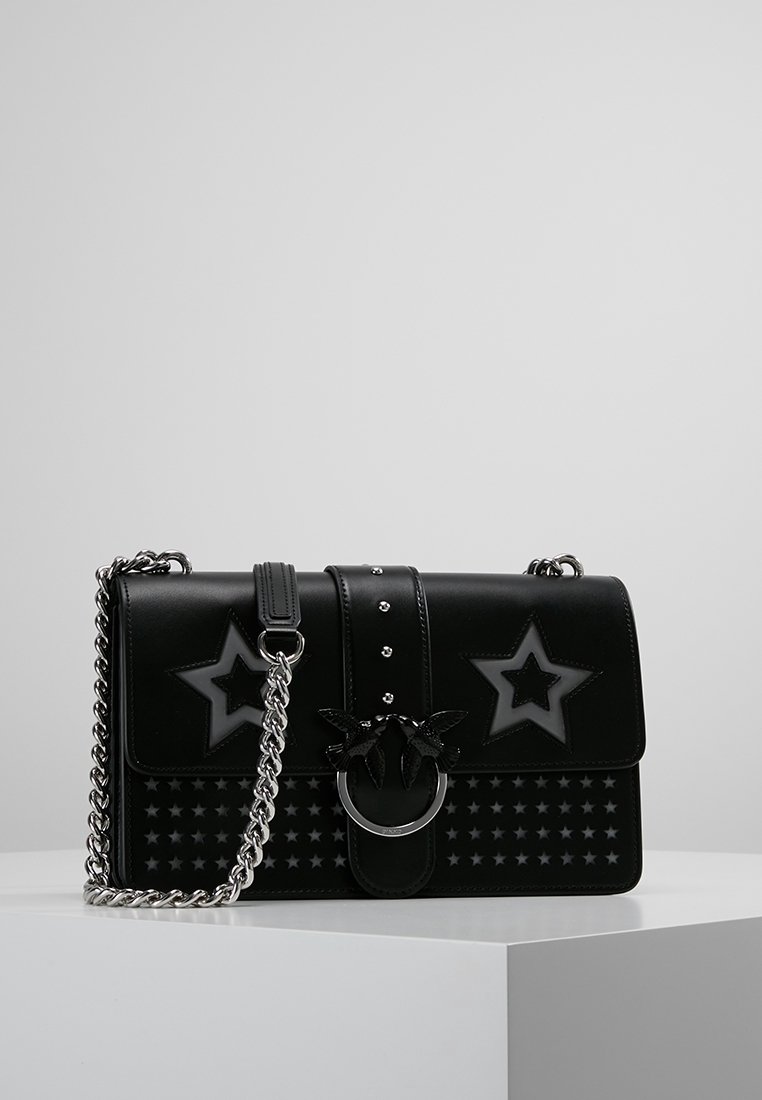 Borsa a tracolla in pelle nera con motivi a stella, tracolla in catena argento e un accentuato anello unico. Presenta una finitura liscia e borchie decorative.