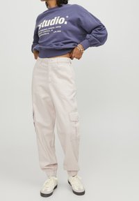 Fialová mikina s bílým potiskem, v kombinaci se světle růžovými cargo kalhotami se stahovacími manžetami a bočními kapsami. Celý vzhled doplňují pohodlné boty.