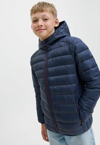 Marinblå pufferjacka med huva, quiltat mönster, framdragkedja och röda detaljer. Har två sidofickor och en figurnära design.