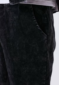 Primo piano della tasca dei pantaloni in corduroy neri e della loro texture, con un accenno di una maglietta grigia sopra.