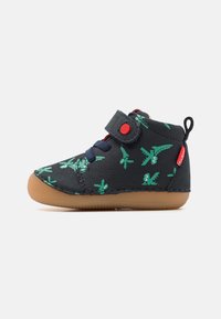 Botte de sneaker noire avec motif d'avion vert, bande velcro, lacets bleus et semelle en caoutchouc gomme. La tige en tissu texturé offre une bonne adhérence.