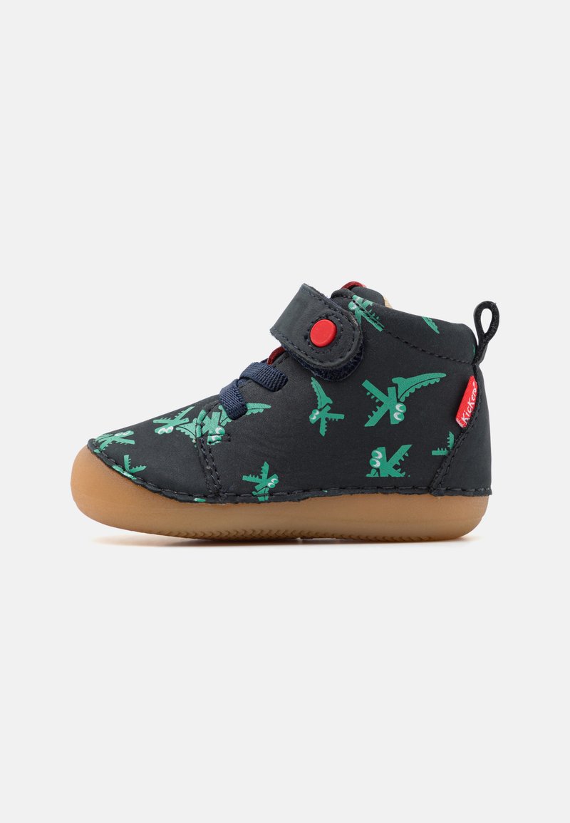 Botte de sneaker noire avec motif d'avion vert, bande velcro, lacets bleus et semelle en caoutchouc gomme. La tige en tissu texturé offre une bonne adhérence.