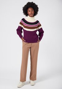 Lila stickad polo tröja med horisontella ränder i kräm, brunt och vinröd. Kombinerad med beige byxor och vita sneakers.