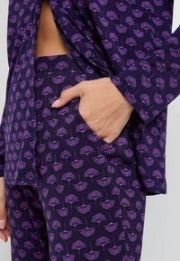 Ensemble de pyjama à motifs violets avec un design floral et des accents violets foncés et roses. Le tissu semble doux avec une coupe décontractée.
