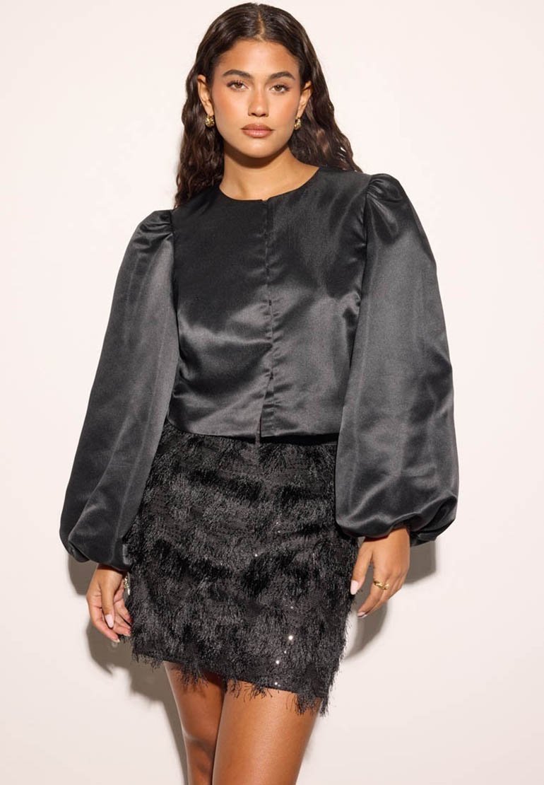 Schwarzes Satin-Crop-Top mit Puffärmeln, kombiniert mit einem schwarzen Minirock aus Federn, der mit Pailletten für zusätzliche Textur verziert ist.