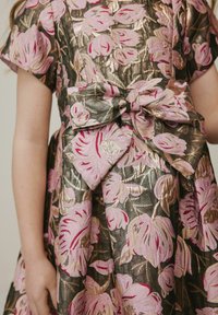 Blumenkleid mit rosa und goldenen Stickereien auf einem dunkelgrünen Stoff, mit kurzen Ärmeln und einer Schleifendetail an der Taille.