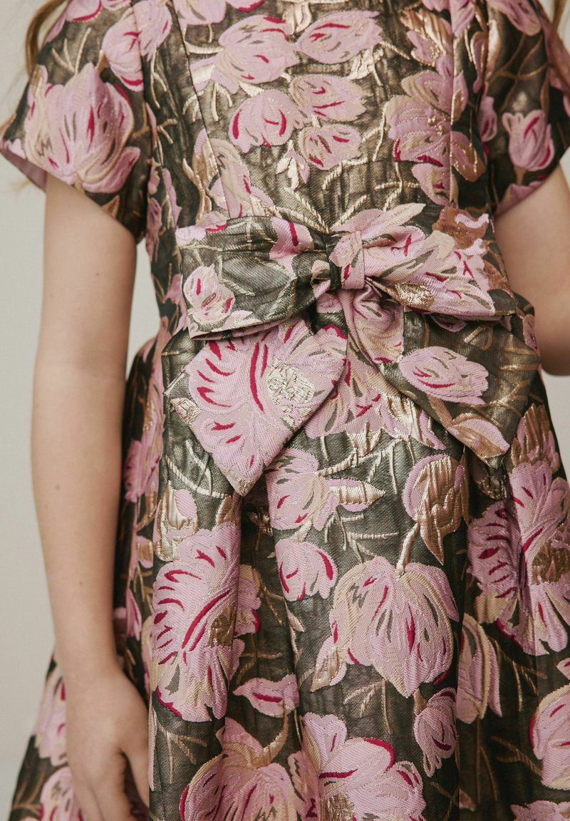 Robe florale avec des broderies rose et or sur un tissu vert foncé, présentant des manches courtes et un détail en nœud à la taille.