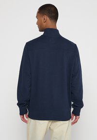 Chaleco de color azul marino con un cuello alto, mangas largas y una textura suave. Presenta un detalle de costura en la parte superior de la espalda.