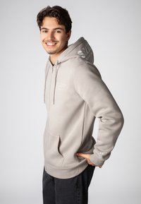 Lichtgrijze zip-up hoodie van zachte stof, met een voorzak, ribgebreide manchetten en bedrukt tekst op de linkerborst en mouw.