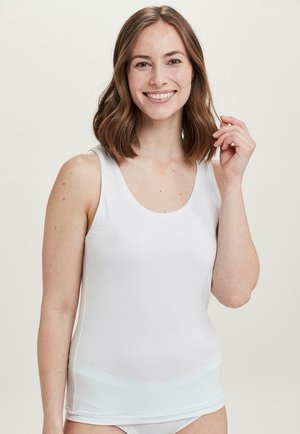 Hvid bomulds tanktop med brede skulderstropper og en rund halsudskæring. Glat tekstur, tætsiddende design. Model, der smiler, let fregnede kinder.