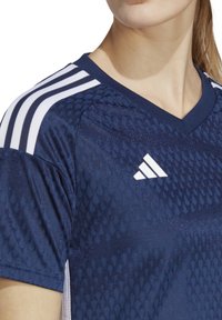 Maglietta atletica blu navy con un design texture, con strisce bianche sulle spalle e logo Adidas sul petto.