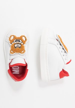 Hvide børnesneakers med røde kanter og et bamsepatch på toppen af snørebåndene, vist fra top- og sidevinkler.
