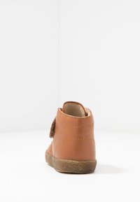 Botte chelsea en cuir marron avec une bande auto-agrippante, bout rond, semelle texturée et coutures visibles. Fini lisse avec un design robuste.