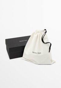 Boîte rectangulaire noire et sac en tissu blanc avec cordon de serrage portant le logo "Massimo Dutti" sur un fond blanc uni.