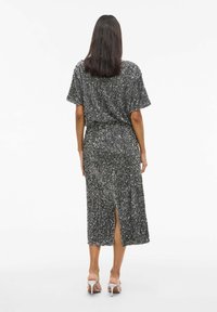 Vestido midi plateado con lentejuelas, mangas cortas y una abertura en la parte trasera. Textura suave; corte holgado; ceñido a la cintura. Combinado con tacones plateados con tiras.